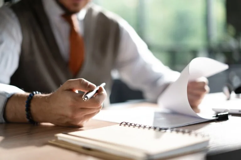 Businessman hands holding pen for working with stack of paper files, searching information, business report papers and piles of unfinished documents in modern office business law faq